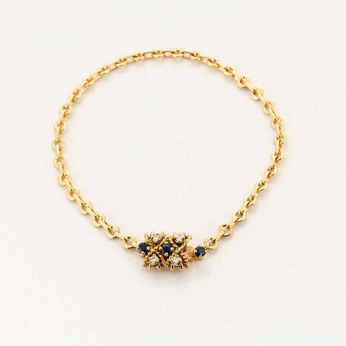 Kierretty keltakultainen rannekoru, jossa safiireja ja timantteja.