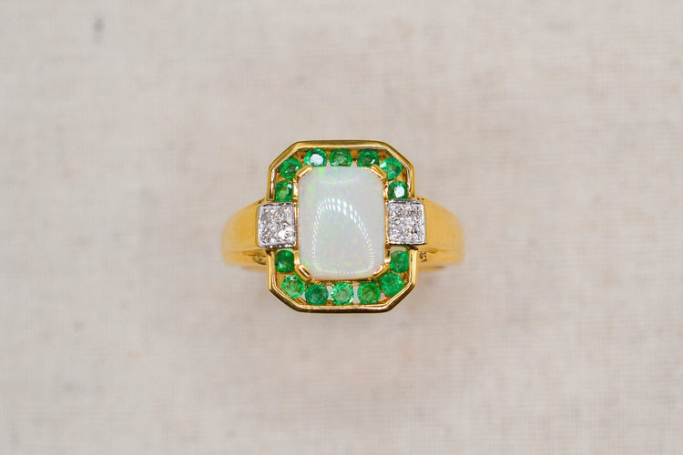 https://cdn.shopify.com/s/files/1/0963/7950/2920/files/bague-en-or-jaune-ornee-d-une-opale-rectangulaire-entouree-d-emeraudes-rondes-en-serti-rail-et-de-diamants-ronds-bague-de-fiancailles.jpg?v=1791882361